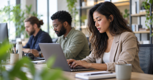 Employees using standard user accounts on laptops in a modern office to reduce administrator access security risks.